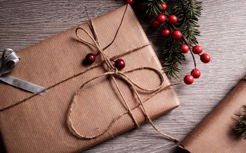 Paquet cadeau emballé de papier kraft et noué d'une ficelle de jute, sur une table en bois près d'un rameau de sapin et de baies rouges