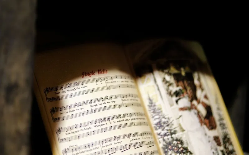 Recueil de chants ouvert à la partition de « Jingle Bells », paroles et portées éclairées d'une lumière chaude, gravure enneigée sur la page voisine