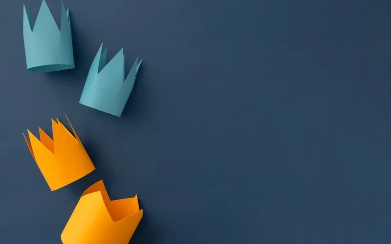 Quatre couronnes en papier découpé, deux bleu turquoise et deux orange, posées sur un fond bleu nuit