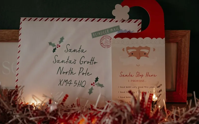 Enveloppe adressée au Père Noël « Santa's Grotto, North Pole », posée près d'une affichette de porte à l'effigie du Père Noël et d'une guirlande