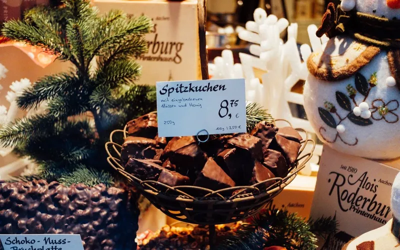 Vitrine de confiserie allemande : corbeille de Spitzkuchen, petits pains d'épices enrobés de chocolat, entre un sapin et un bonhomme de neige en feutre
