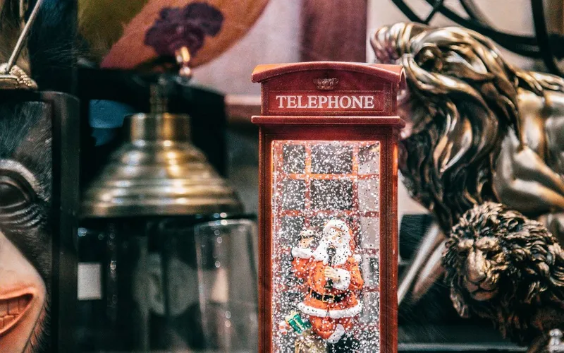 Cabine téléphonique rouge miniature de style britannique abritant un Père Noël sous une neige artificielle, au milieu de bibelots d'antiquaire