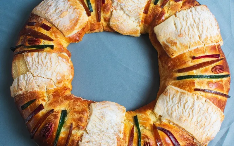 Couronne briochée des Rois vue du dessus, décorée de fruits confits verts et rouges, de noix de pécan et de plaques de pâte sucrée