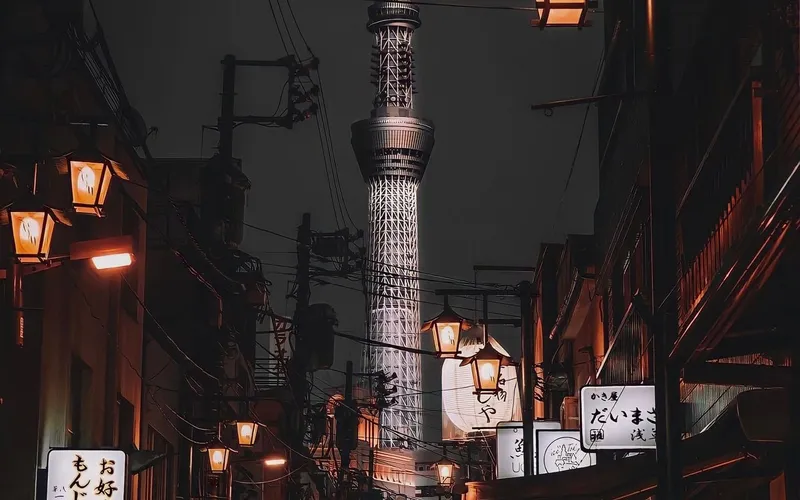 Ruelle de Tokyo le soir, lanternes allumées et enseignes en japonais, avec la tour Tokyo Skytree illuminée au bout de la rue