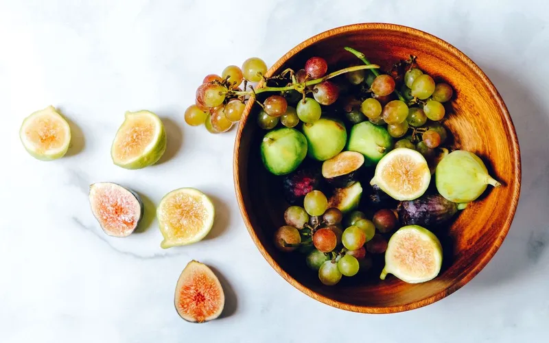Coupe en bois remplie de figues fraîches et de grappes de raisin, figues coupées en deux posées à côté sur un plan de marbre