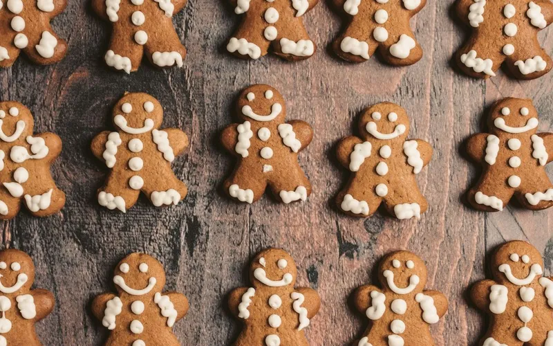 Rangées de bonshommes en pain d'épices décorés de glace royale blanche, posés sur une planche en bois sombre