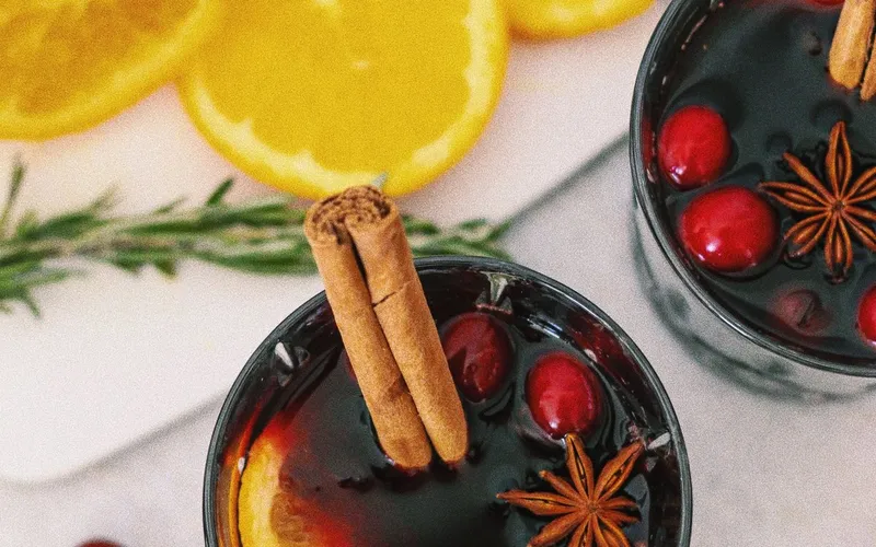 Deux verres de vin chaud vus du dessus, avec bâton de cannelle, anis étoilé, canneberges et rondelle d'orange, près d'oranges tranchées et d'un brin de romarin